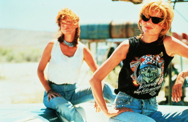 Thelma and Louise sit on top of the Thunderbird in all their bad ass glory, taunting the truck driver.