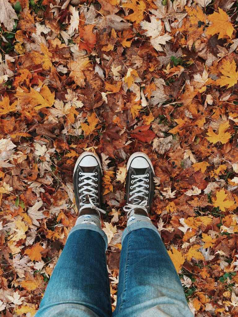 A pair of sneakered feet in autumn leaves.
